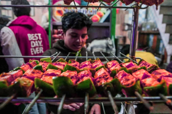 A street vendor grilling delicious paneer tikka skewers with green peppers at a bustling Delhi street food stall, with people enjoying the vibrant scene.