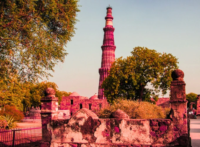 Qutub Minar in Delhi surrounded by historical ruins and lush trees during sunset