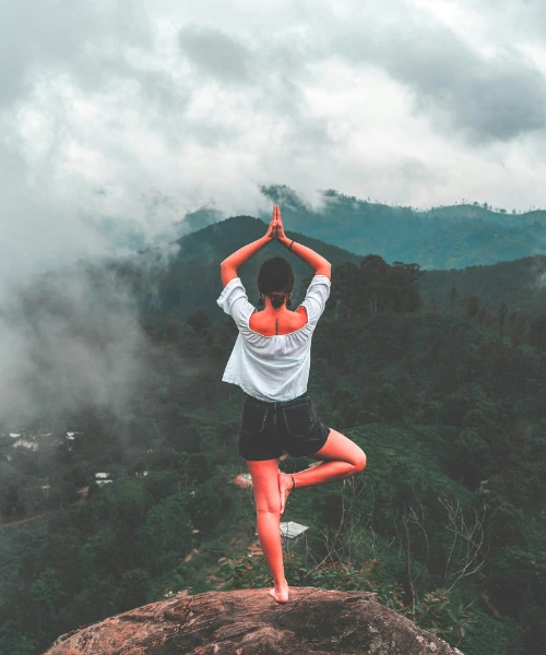 Woman practicing yoga on a mountain cliff surrounded by mist and forest